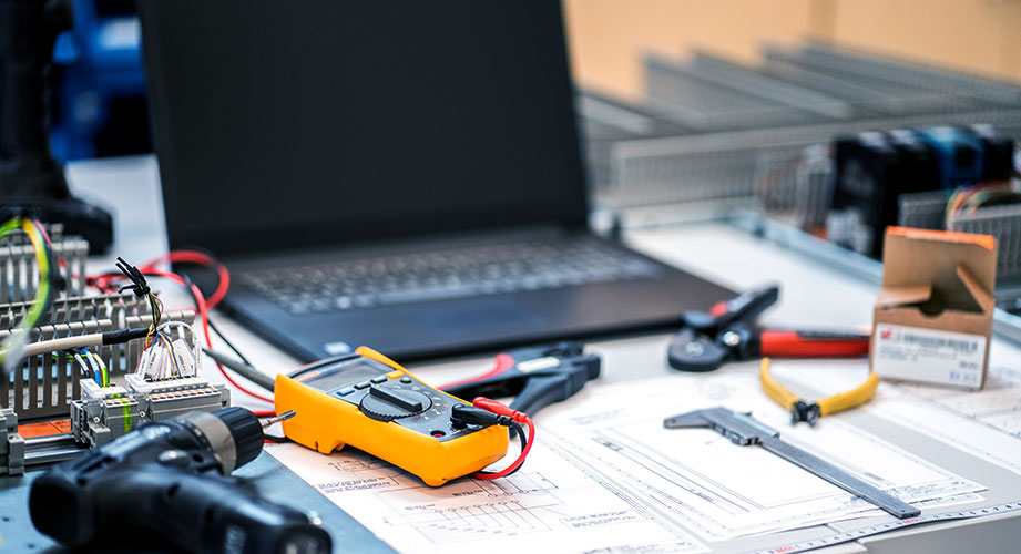 Työpöytä jolla on piirustukset, tietokone ja erilaisia työvälineitä.