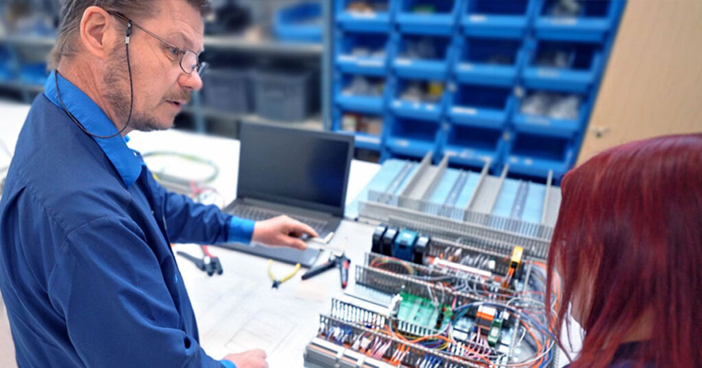 Kaksi työntekijää keskustelevat työpöydän ja kokoonpanon äärellä.